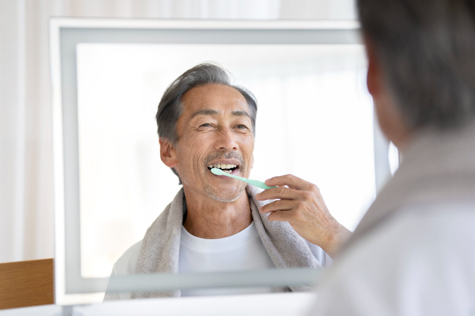 歯周病の予防で鏡を見ながら丁寧に歯みがきをしている男性