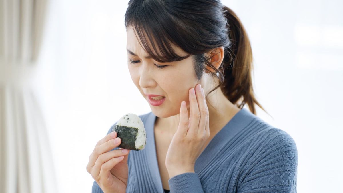 おにぎりを食べる時に痛む顎をおさえる女性