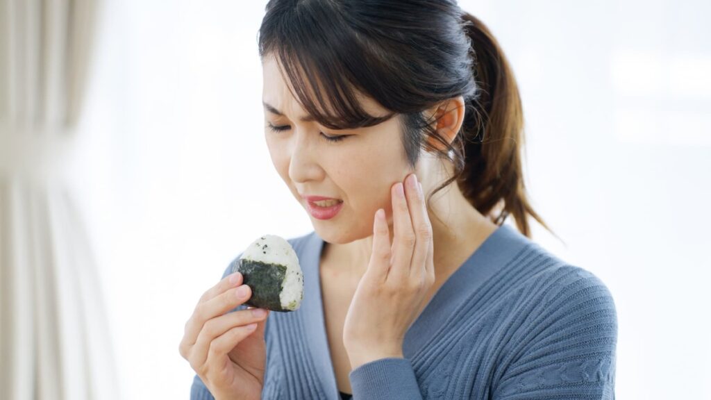 おにぎりを食べる時に痛む顎をおさえる女性